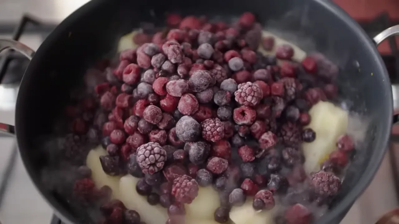 Top-down close-up of a steaming pan filled with frozen mixed berries piled on pear pieces