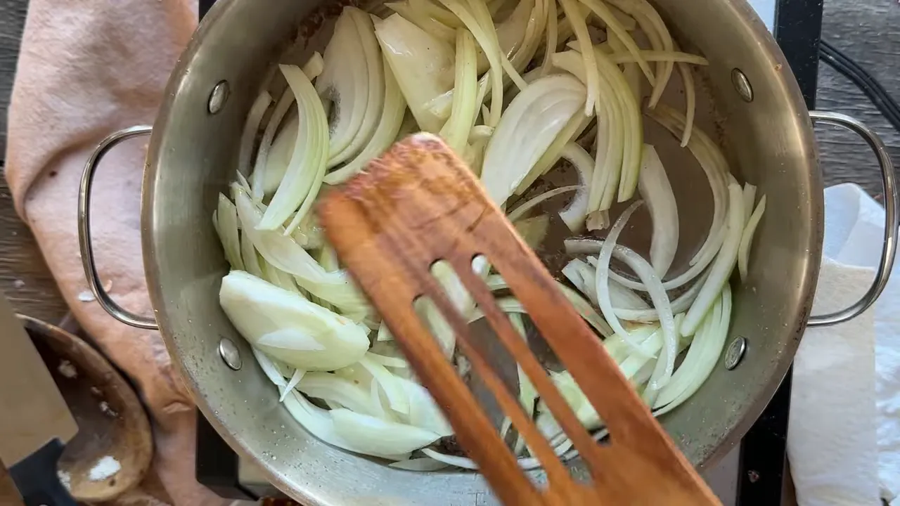 thinly sliced yellow onions in a skillet with a wooden spatula