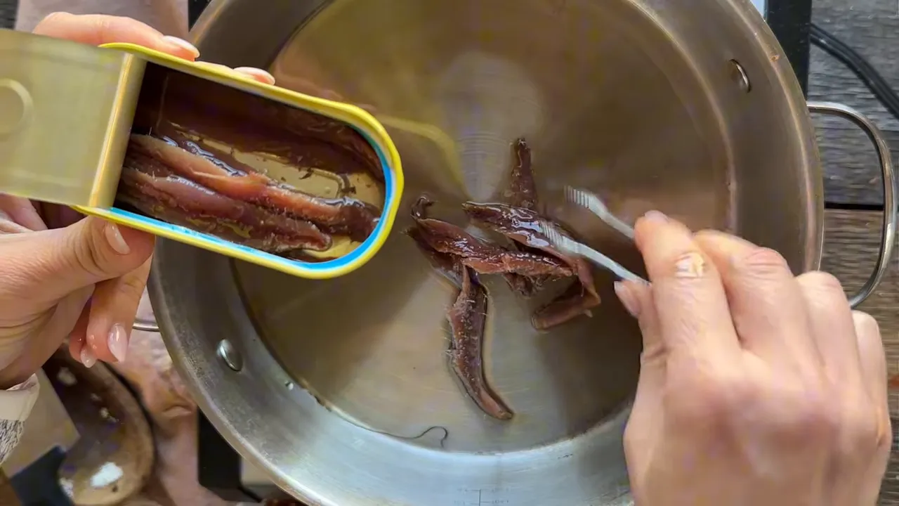 anchovy fillets being placed into a skillet of warm oil