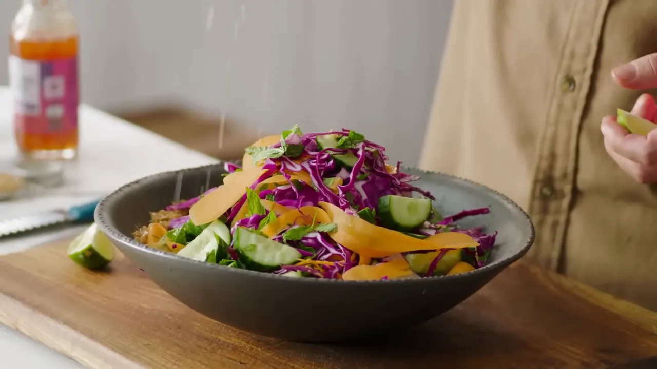 Indonesian-style leftover salad in a bowl with red cabbage, cucumber ribbons and lime being squeezed