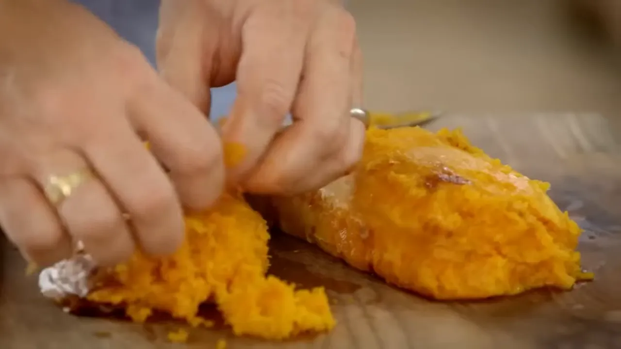hands breaking and mashing roasted orange squash on a wooden board