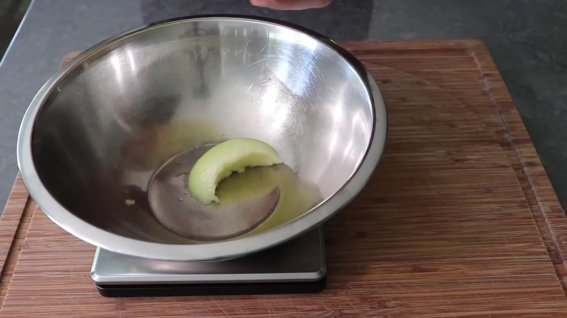 Scooping ripe honeydew into a bowl on a scale