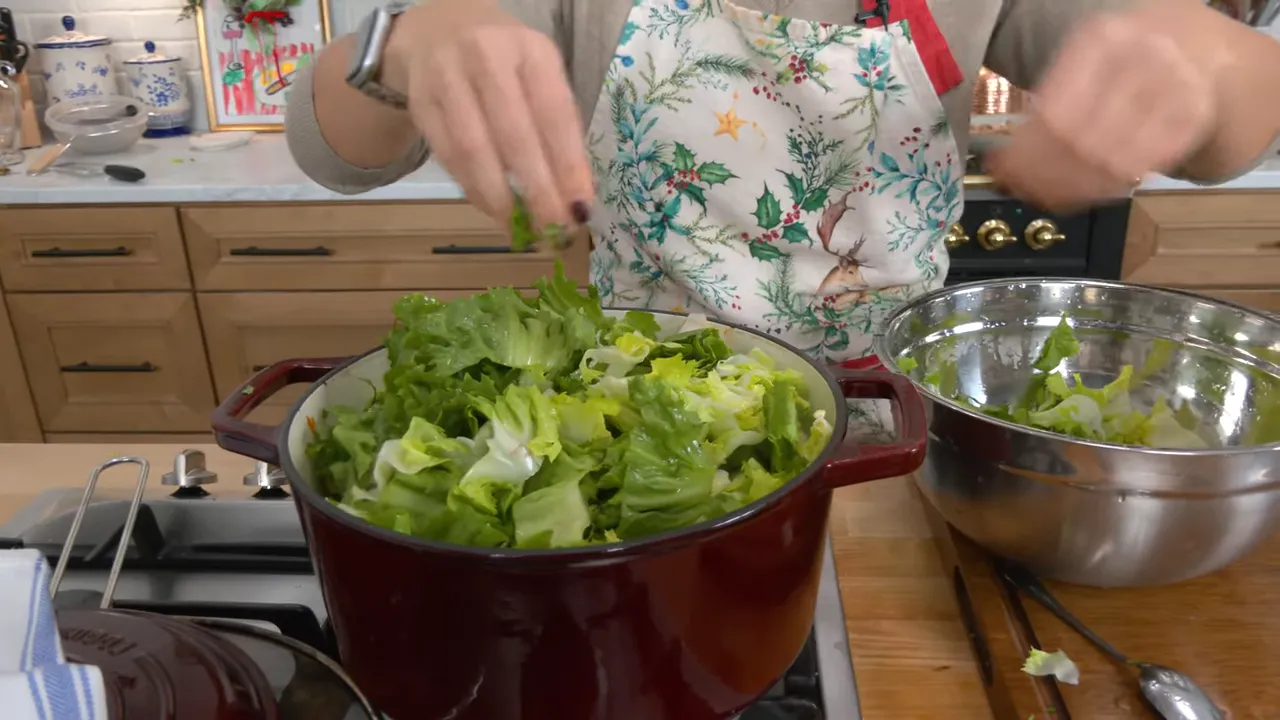 close-up of chopped escarole being added into a red pot of soup