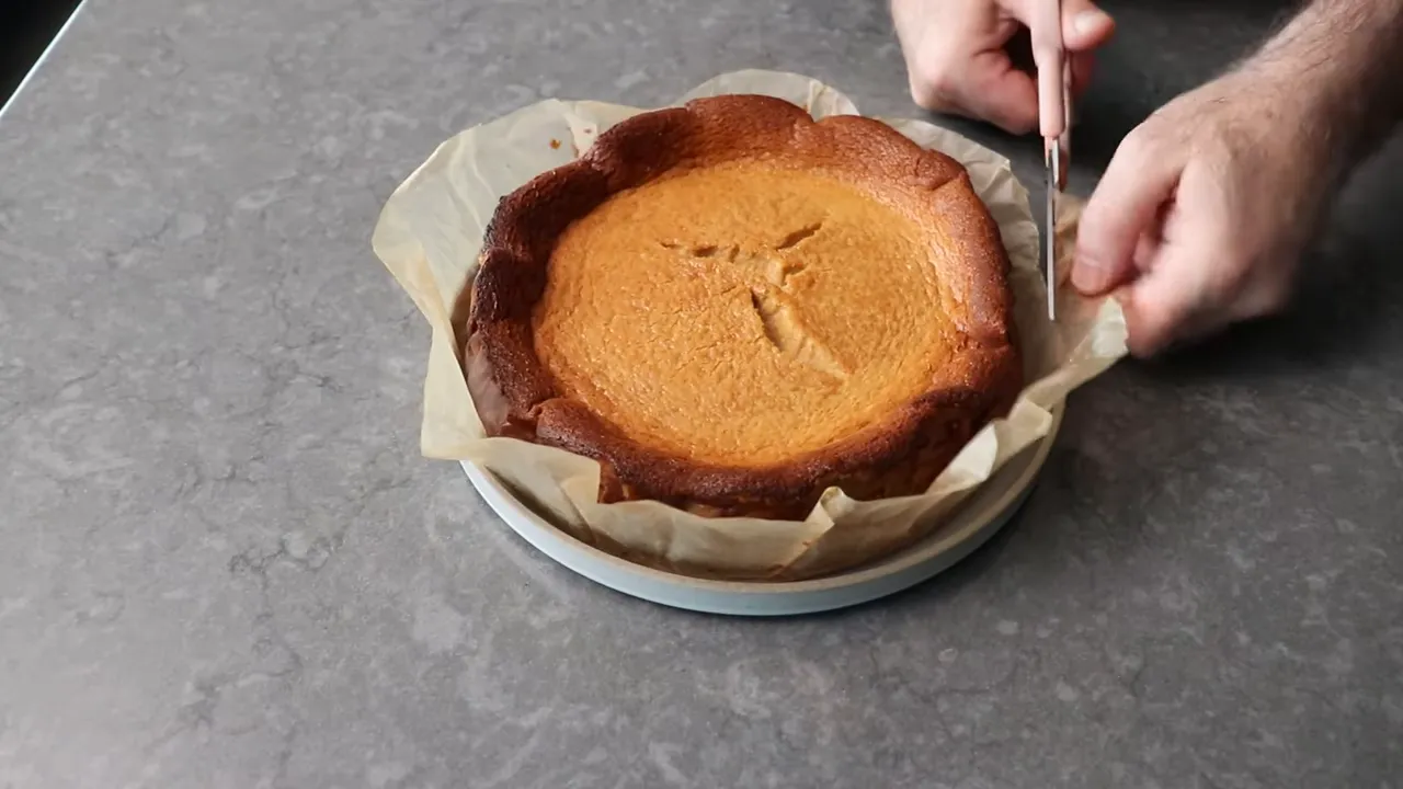 Hands using scissors to trim excess parchment paper from around a gingerbread Basque cheesecake