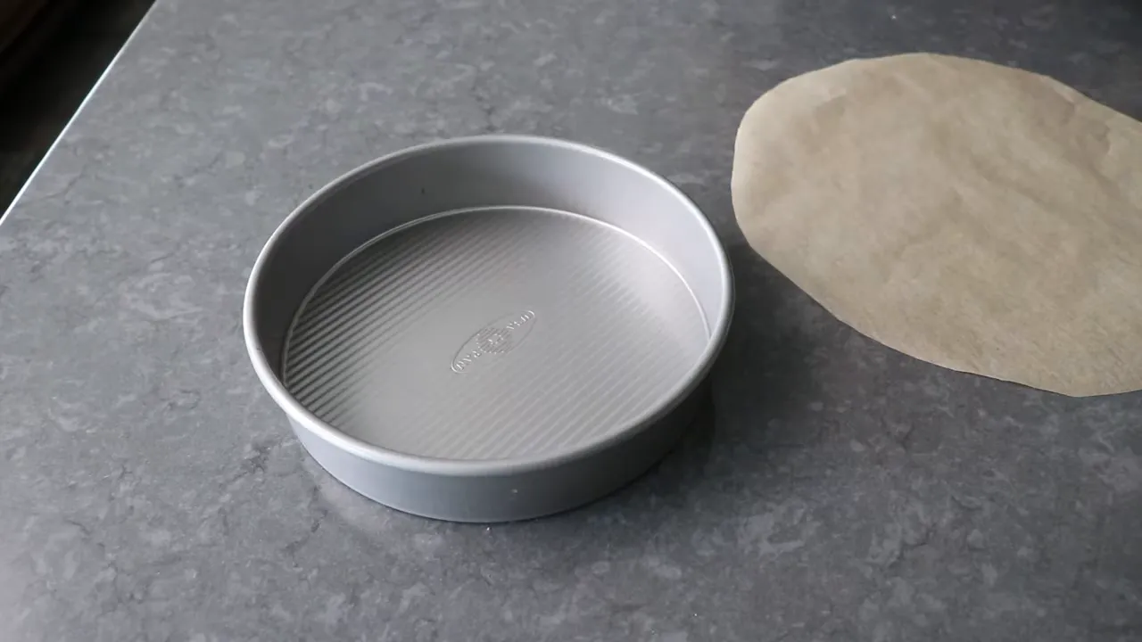 Round cake pan next to a circular sheet of parchment paper on a countertop