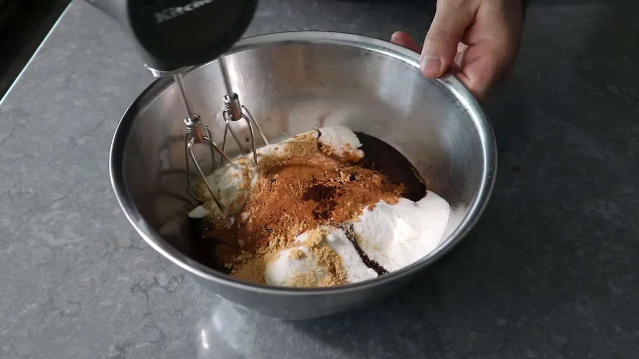 handheld electric mixer beginning to beat gingerbread Basque cheesecake ingredients in a metal bowl