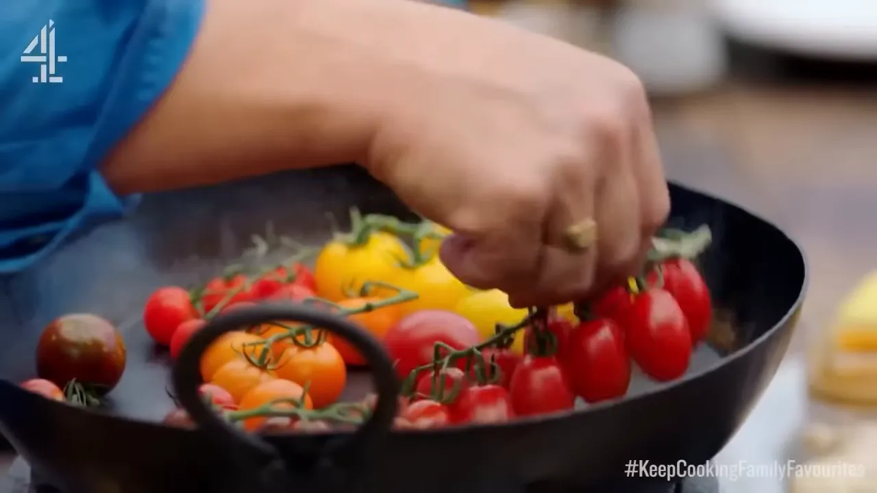 Hand adding cherry tomatoes into a hot black pan for charring