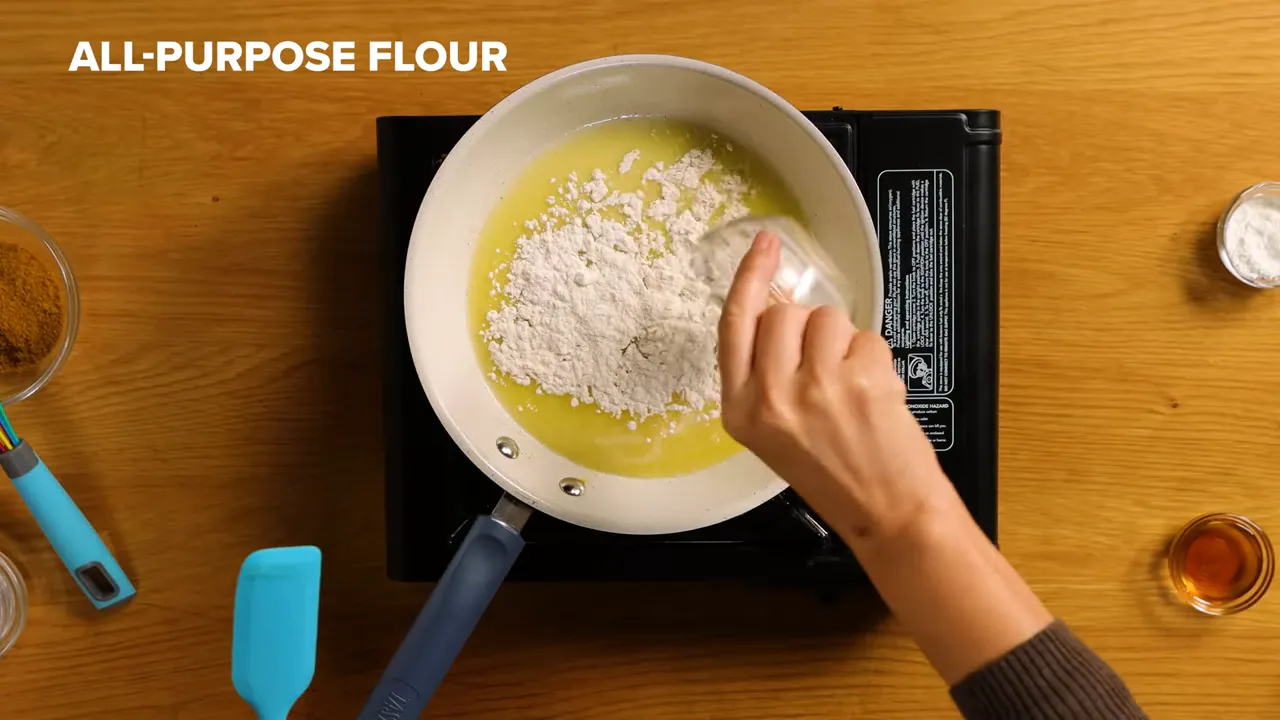 Top-down shot of flour being poured into melted butter in a pan to make a roux