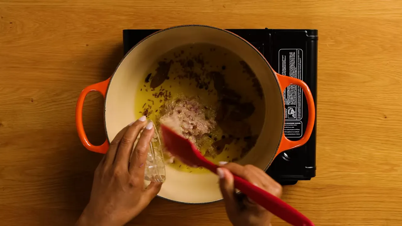 Pouring onion and garlic paste into a pot with bloomed spices and oil