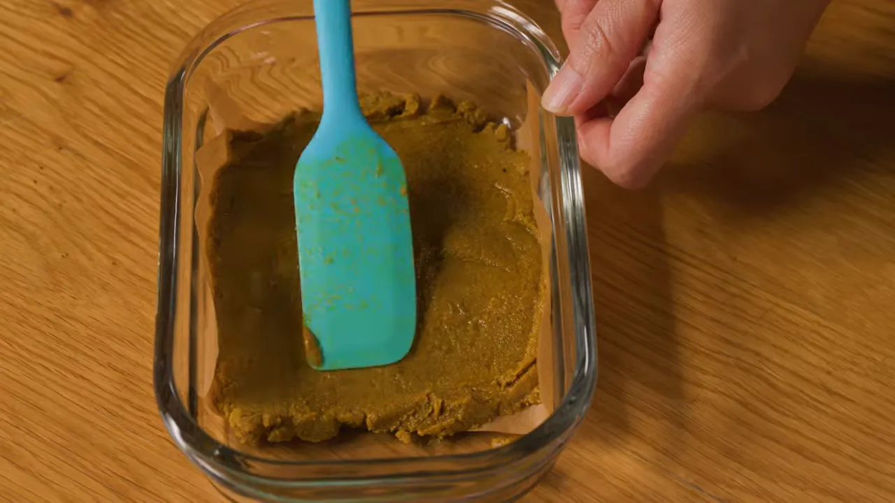 Top view of a curry roux block pressed flat in a glass container with a blue spatula
