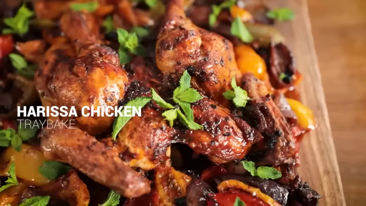 close-up of harissa-roasted chicken drumsticks on a tray with roasted peppers and mint leaves