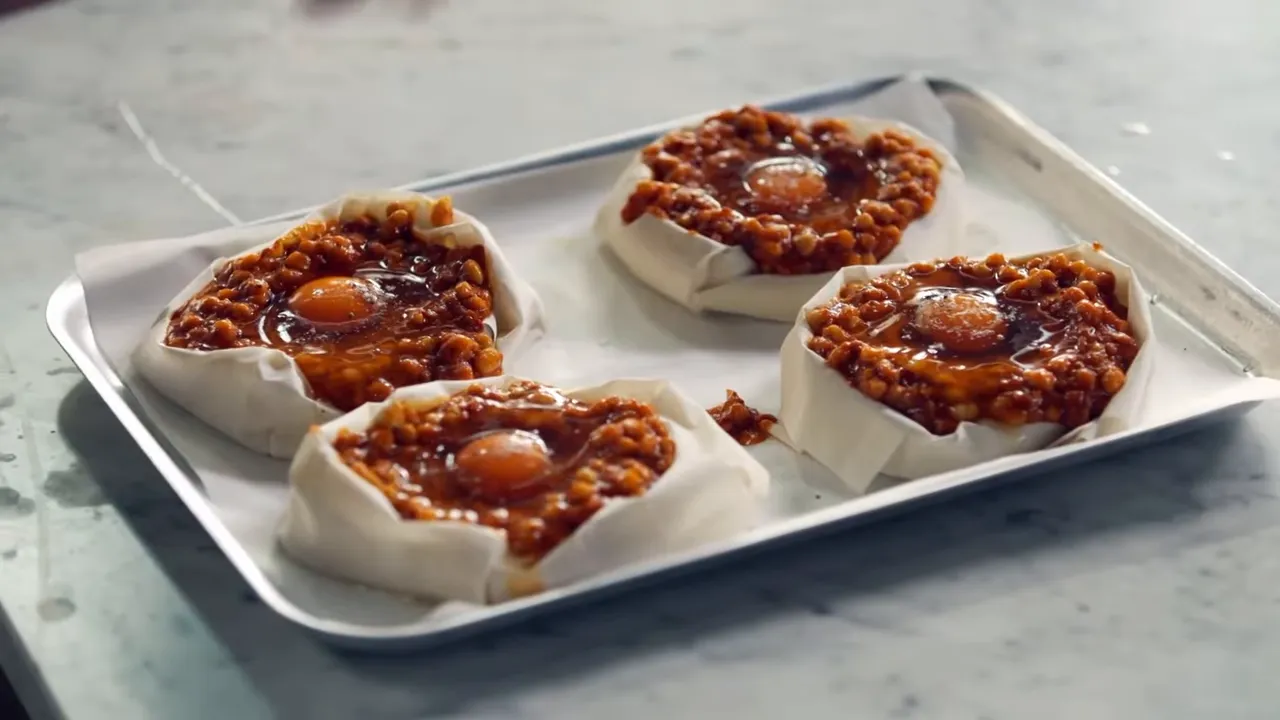 Four filo pastry nests filled with seasoned beans and eggs on a parchment-lined baking tray.