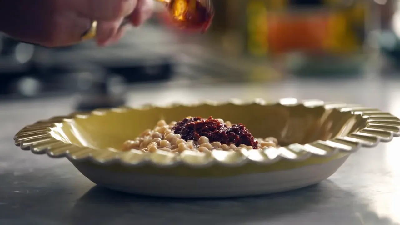 spoonful of harissa being added to beans in a yellow dish