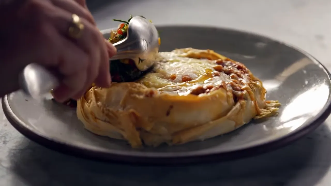 Tongs spooning a dill and pepper salsa onto a plated filo egg and bean nest ready to serve.