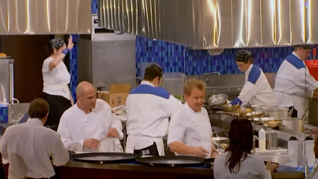 Wide view of a hectic dinner service with multiple cooks working at stations and a head chef moving through the line