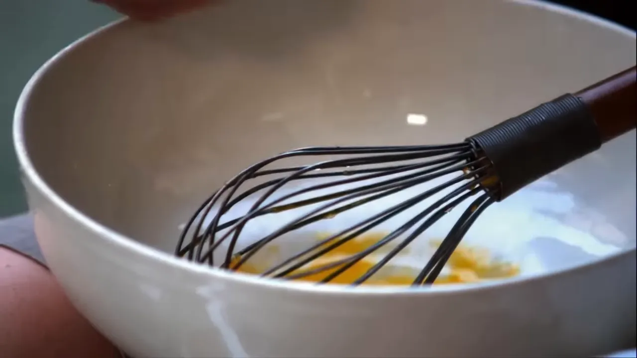 white mixing bowl with a whisk and egg yolks/whites at the bottom
