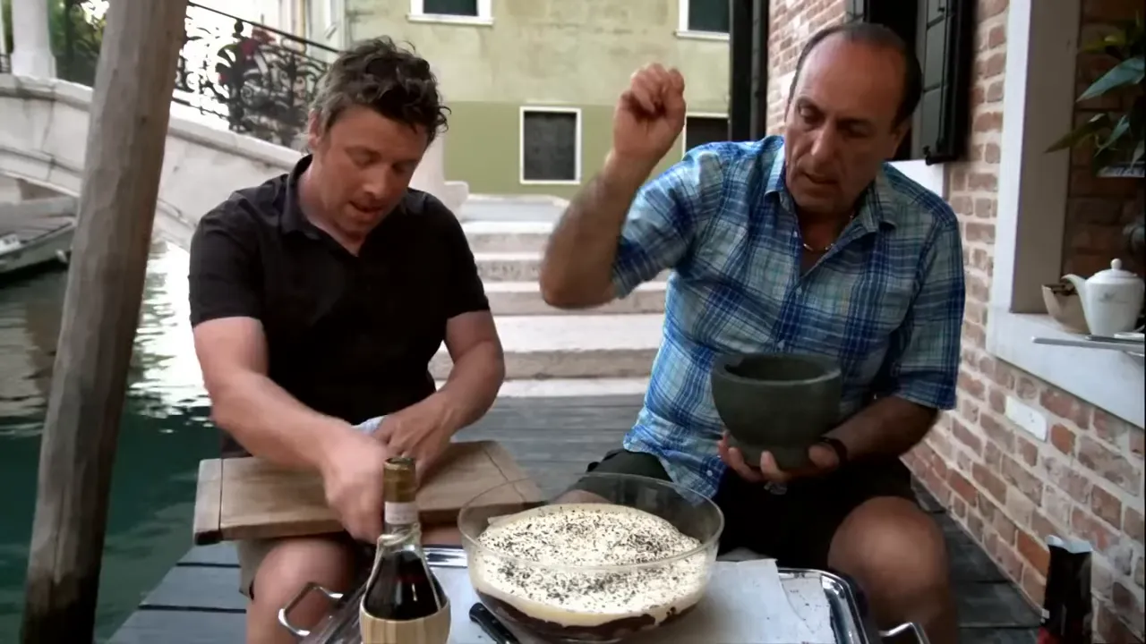 Completed tiramisu in a glass bowl topped with grated chocolate and coffee flecks while final seasoning is added
