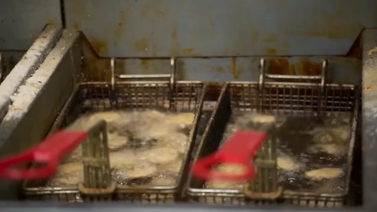 Commercial deep fryer with two baskets frying food and bubbling oil, showing grease on lip of fryer