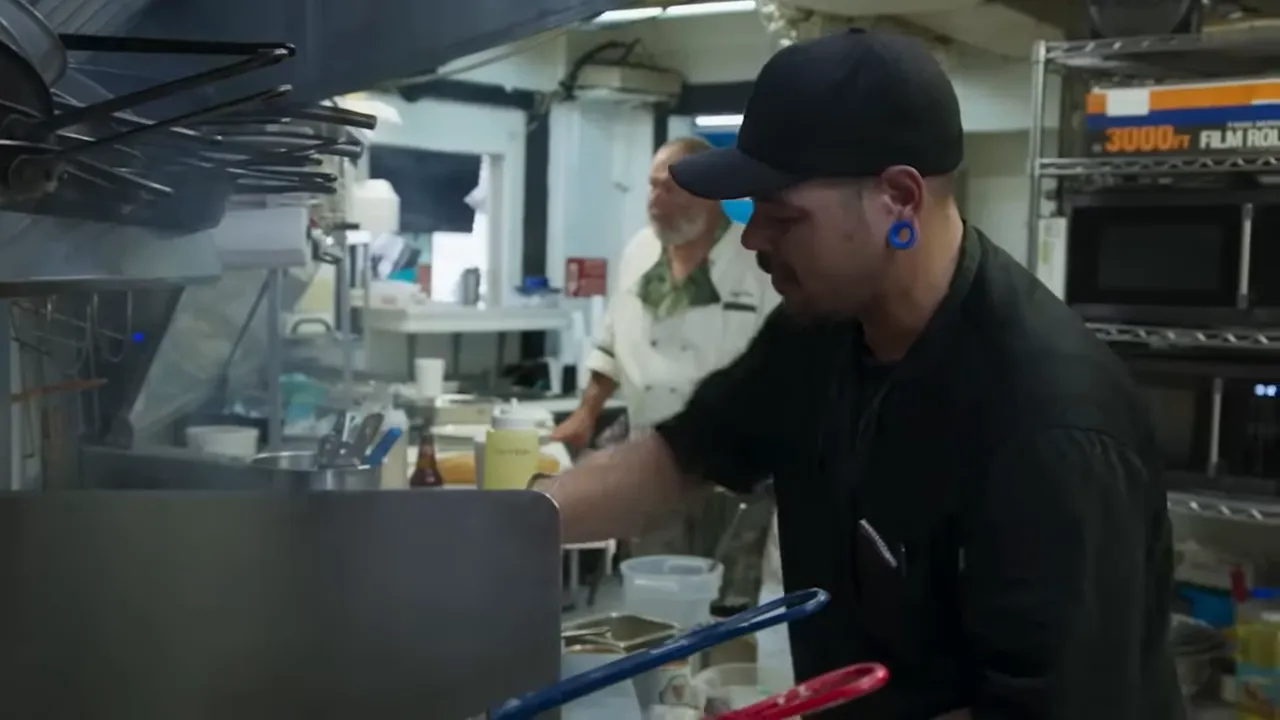 Cook concentrating on a busy kitchen line with utensils and pans visible