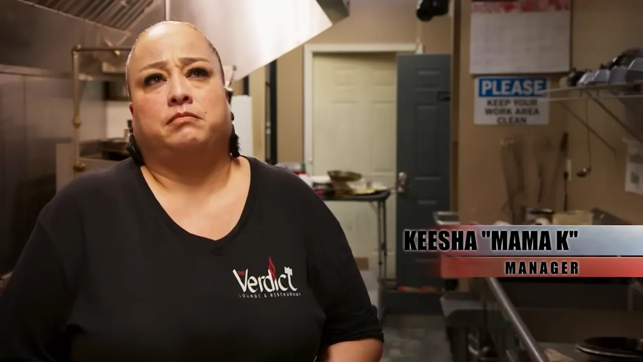 Kitchen scene showing a manager in front of stainless equipment and a 'Please keep your work area clean' sign