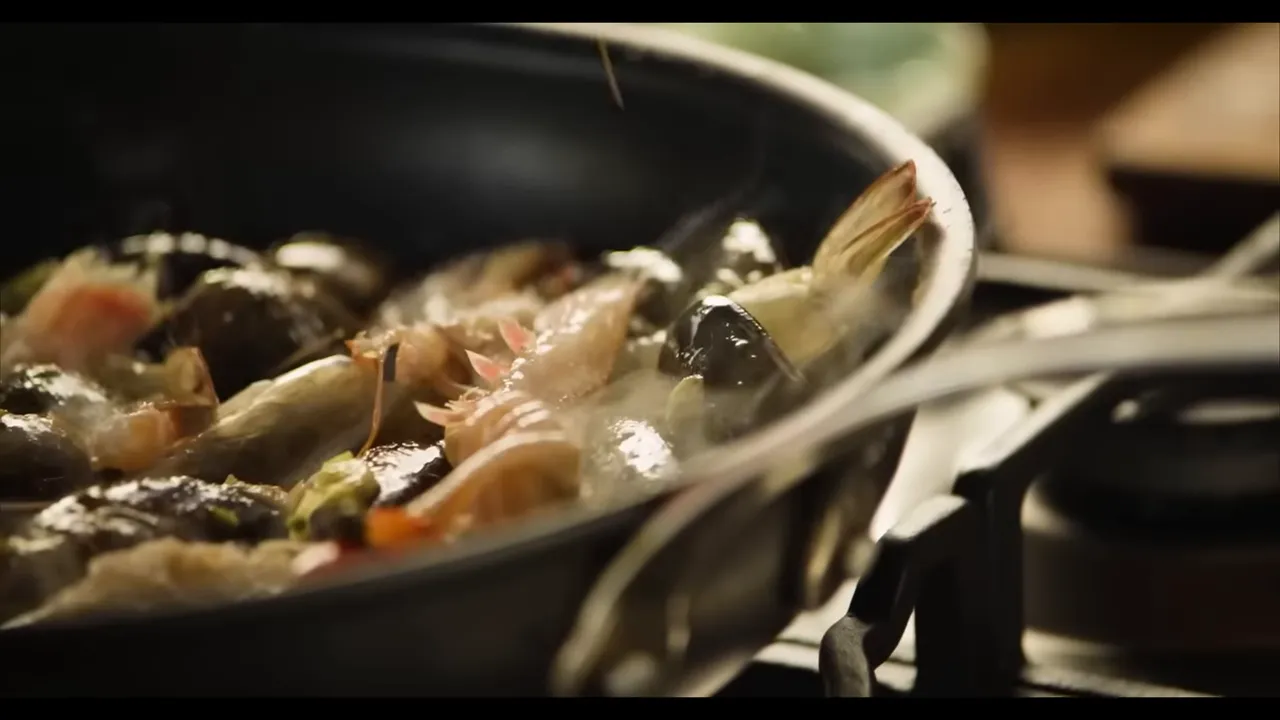 prawns and mussels simmering together in a skillet with steam