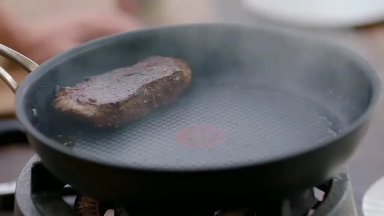 seared sirloin steak cooking in a frying pan with steam rising