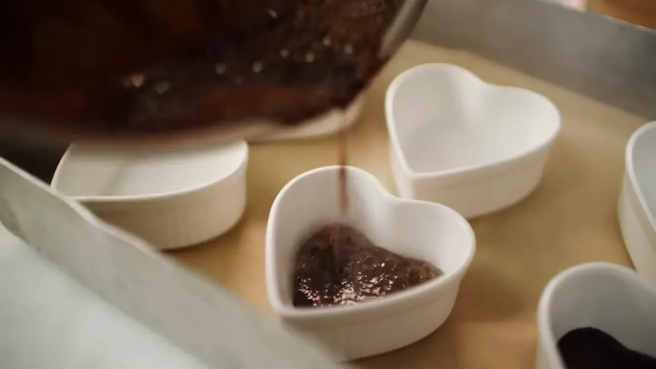Hot caramel being poured into a heart-shaped white ramekin