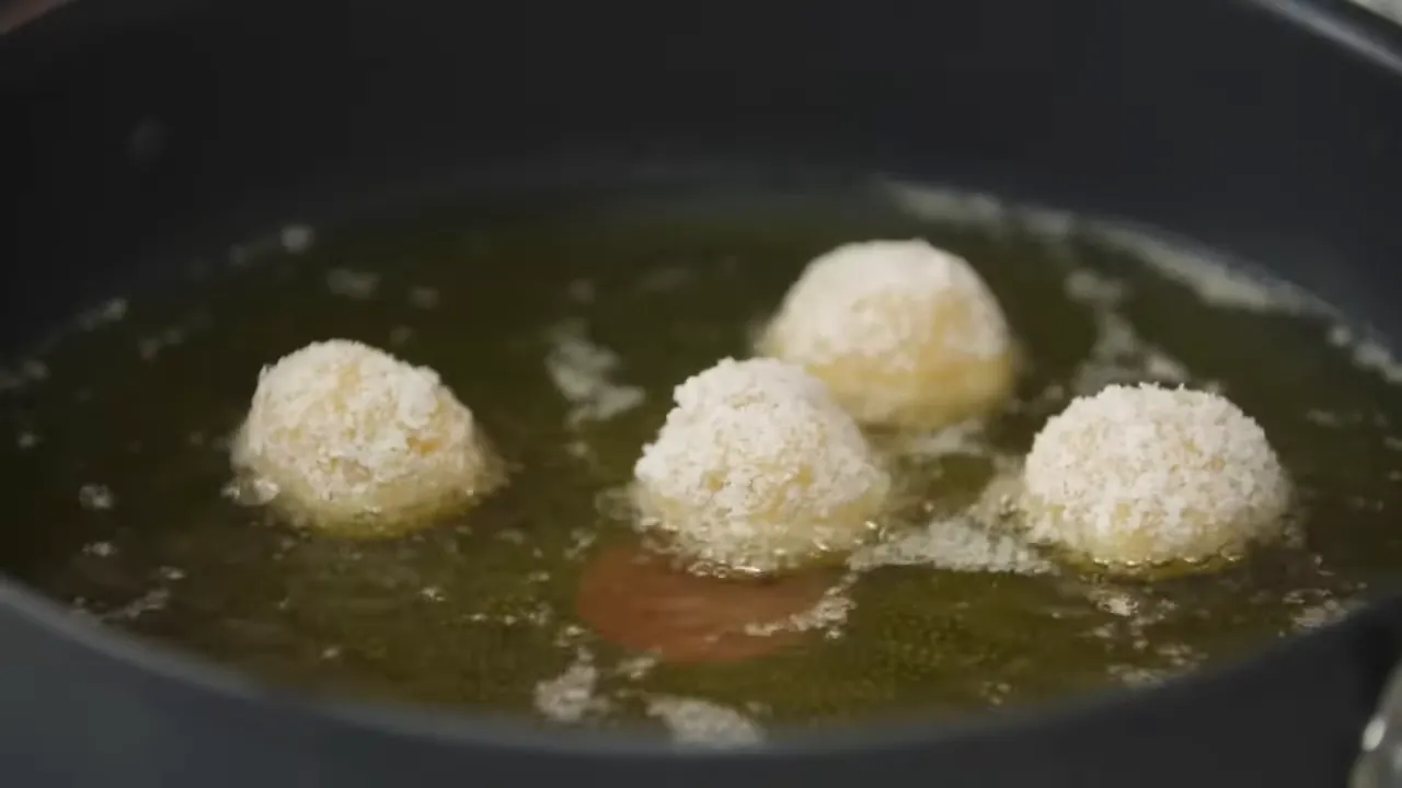 four breadcrumb-coated potato balls frying in a pan of hot oil