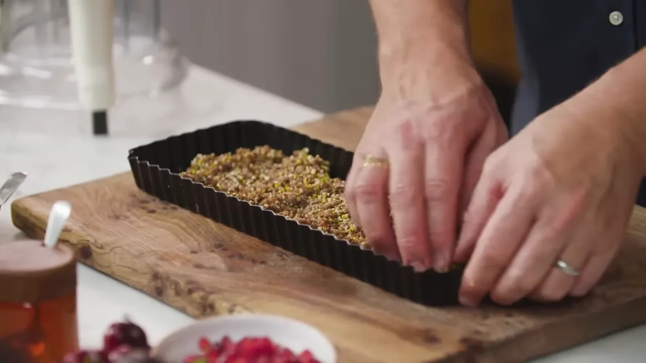 close-up of hands compacting a fig and nut crumb mixture into a fluted rectangular tart tin