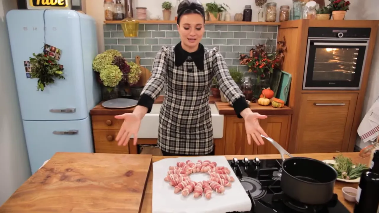 Finished pigs-in-blankets wreath on parchment paper in a kitchen, with the cook gesturing over it.