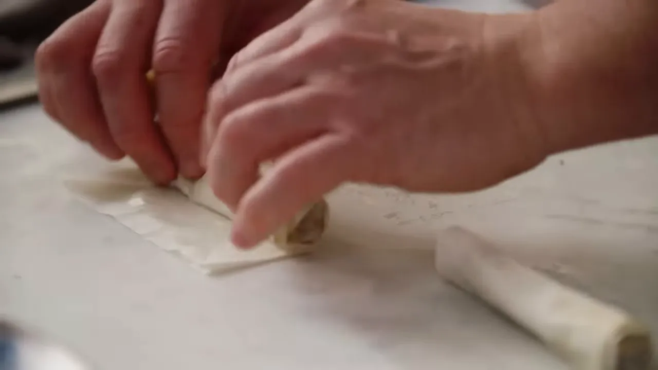 close-up of hands rolling a lamb-filled filo cigar on a marble surface
