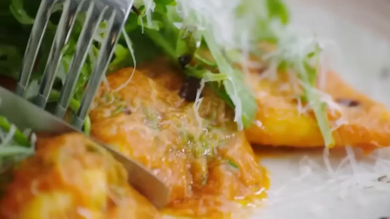 Fork and knife cutting into butternut and ricotta ravioli to reveal filling