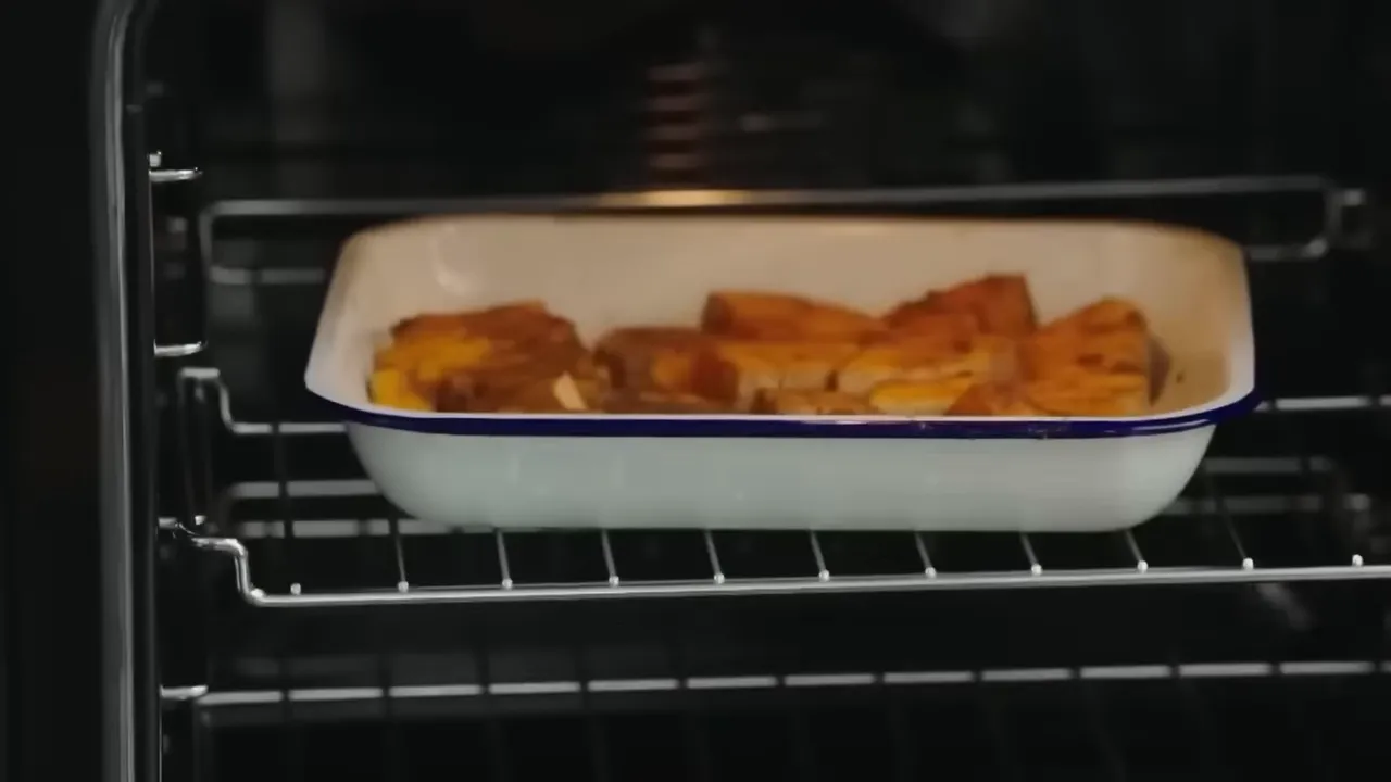 White enamel baking dish of butternut squash cubes roasting on an oven rack.