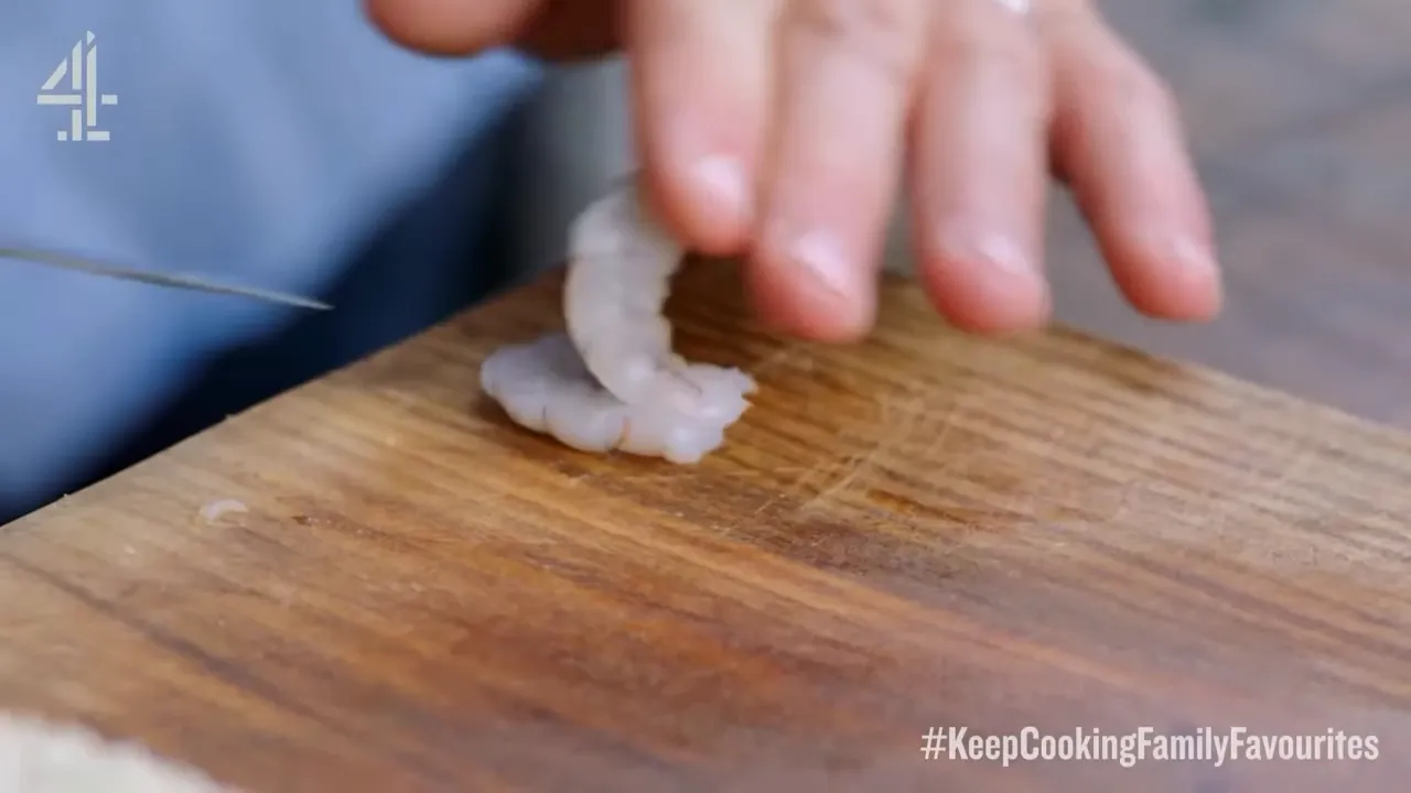 close-up of raw prawns being sliced on a wooden cutting board