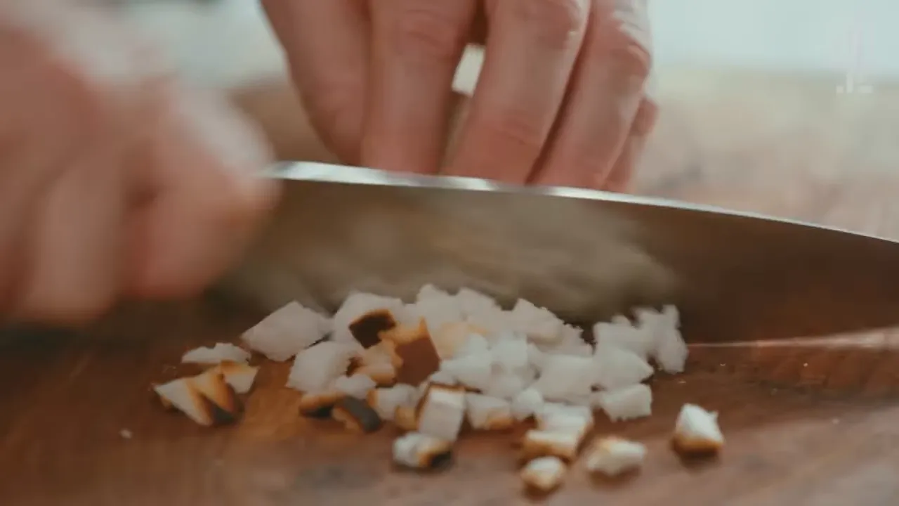 Close-up of a chef's knife dicing browned breadcrumb-sized pieces on a wooden board