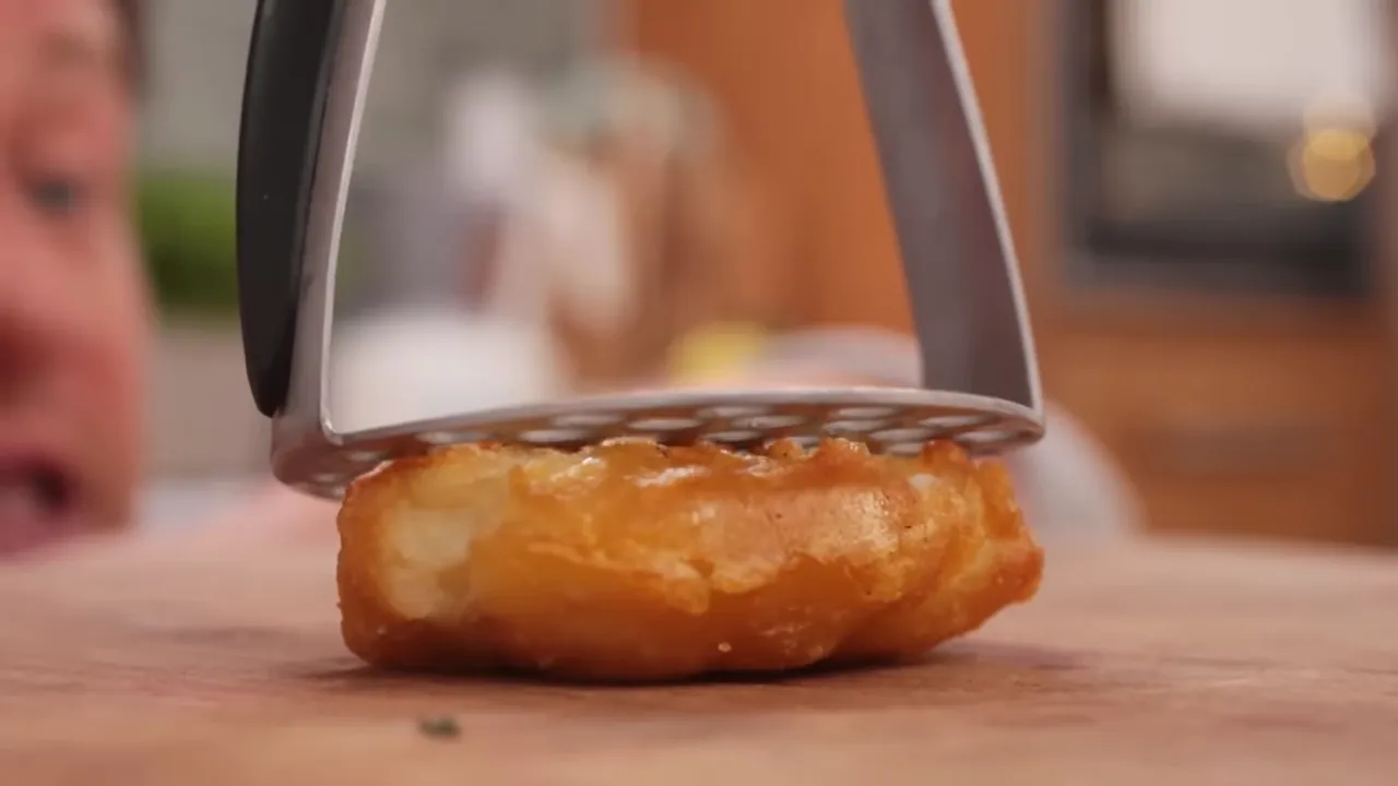 Close-up of a potato being smashed with a masher to increase surface area for crisping
