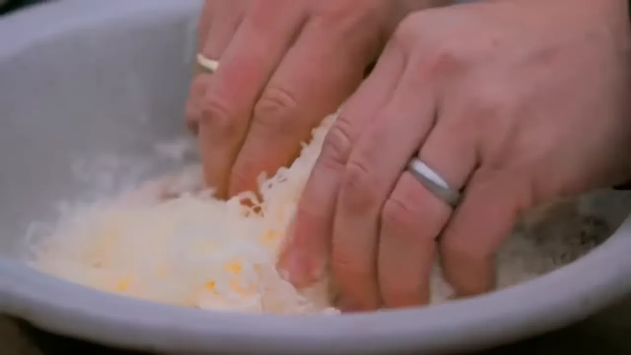 hands pressing and mixing oat and cheese crumble topping in a bowl
