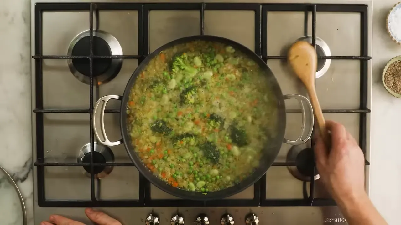 Overhead shot of a pan of vegetable minestrone with visible green pesto dollops and a wooden spoon.