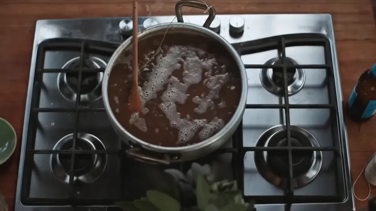 top-down view of a pot of soup simmering on a gas hob with a wooden spoon