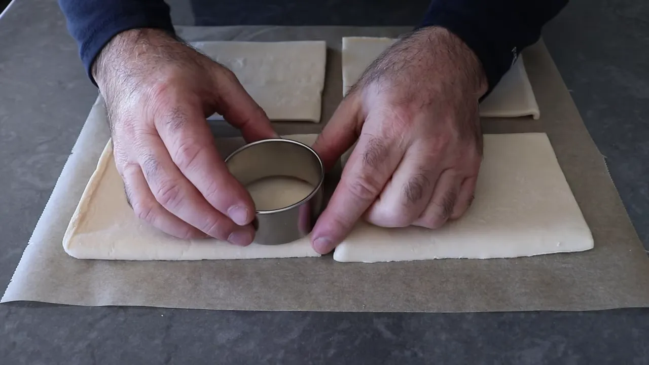Hand pressing a round cutter into puff pastry to cut a circular center