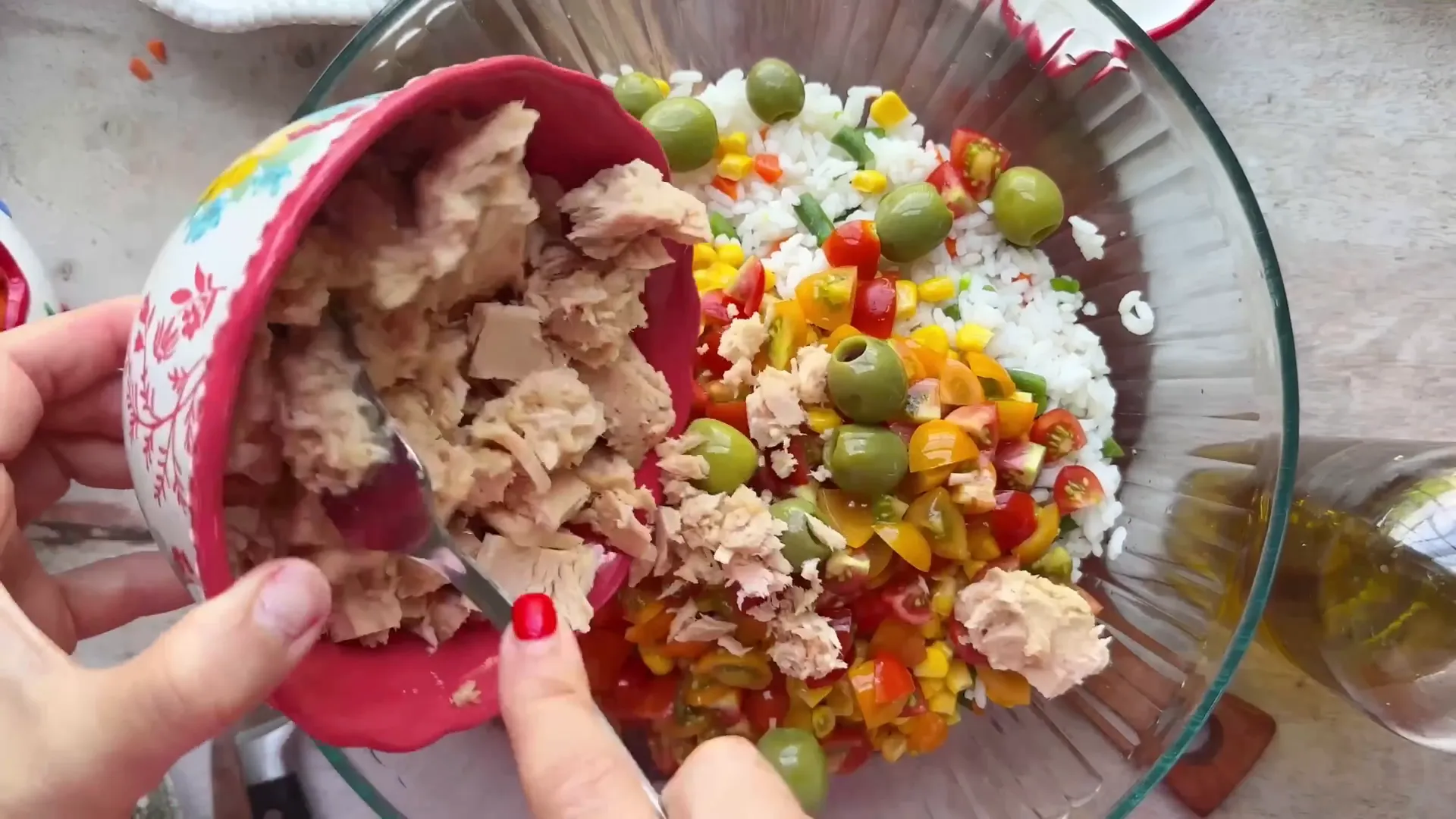 Mixing cooled rice with corn, tomatoes, olives, and tuna