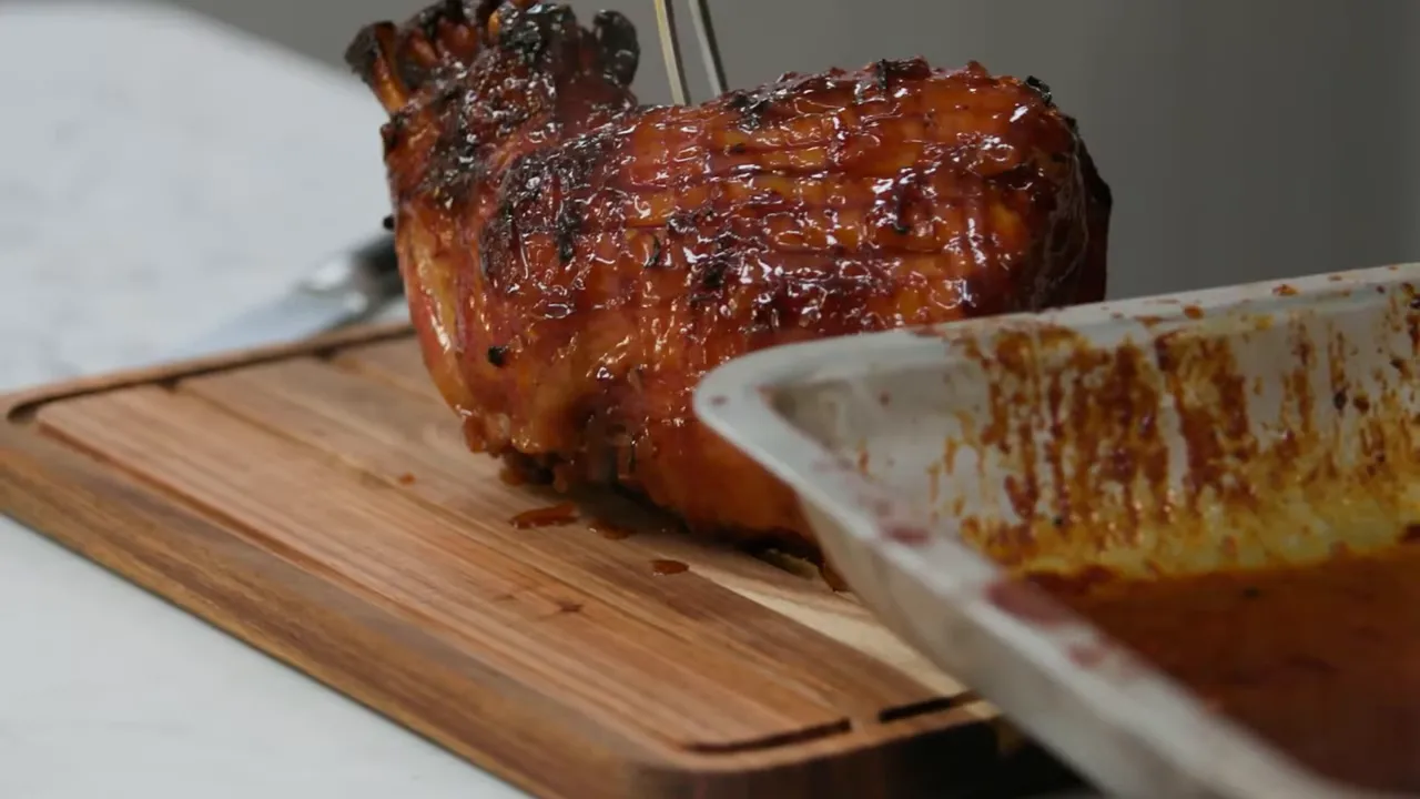 glazed gammon on wooden cutting board beside roasting tray