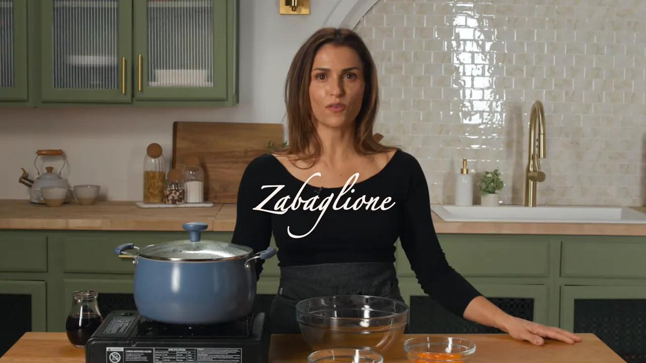 Host at a kitchen counter with a covered pot and bowls; on-screen text reads 'Zabaglione'