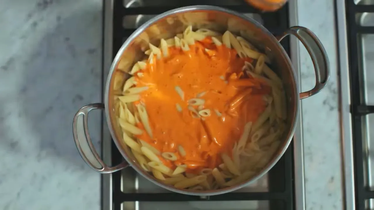 Overhead view of a pot on the stove with penne pasta and orange roasted‑pepper sauce