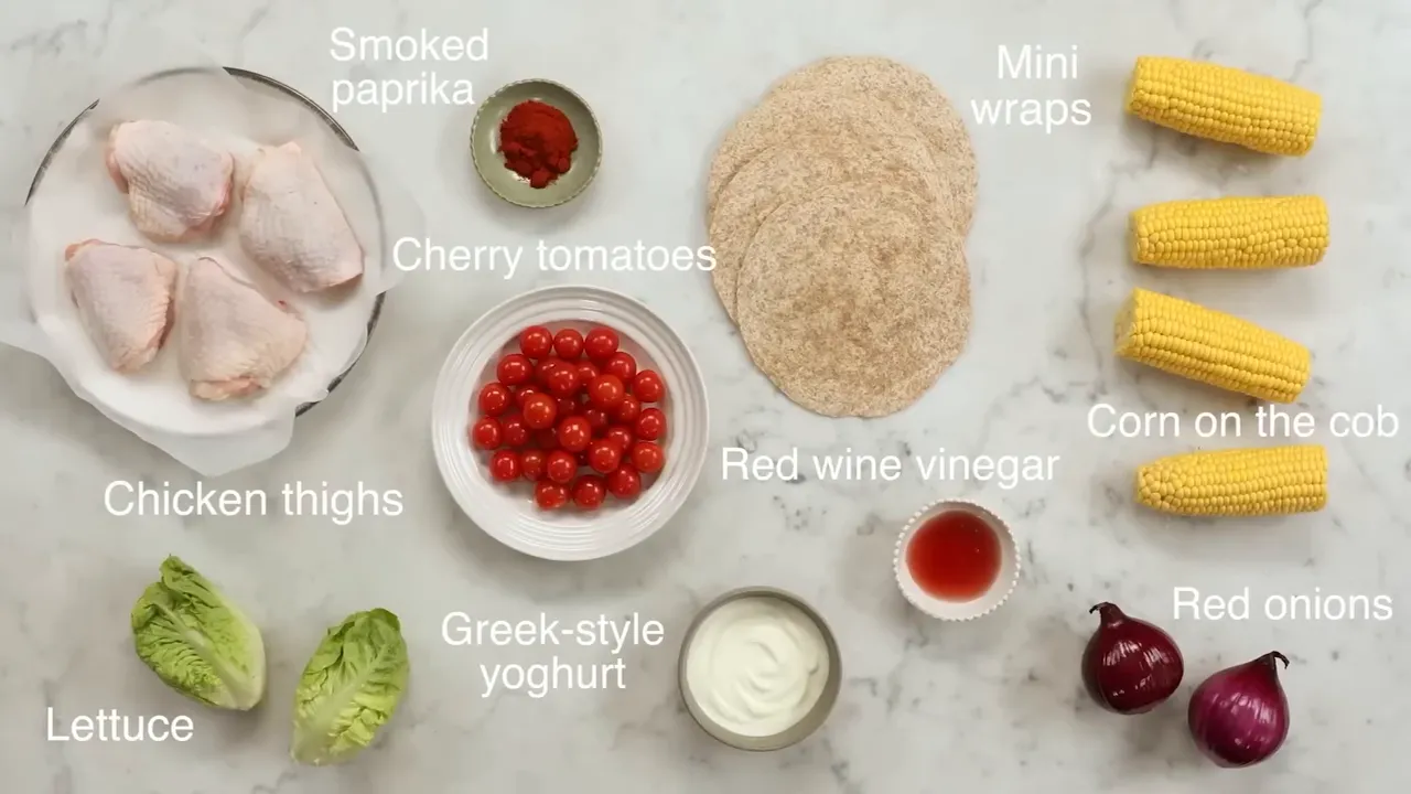 Overhead shot of ingredients for one-tray chicken: chicken thighs cherry tomatoes mini wraps corn lettuce red onions smoked paprika red wine vinegar and greek yoghurt
