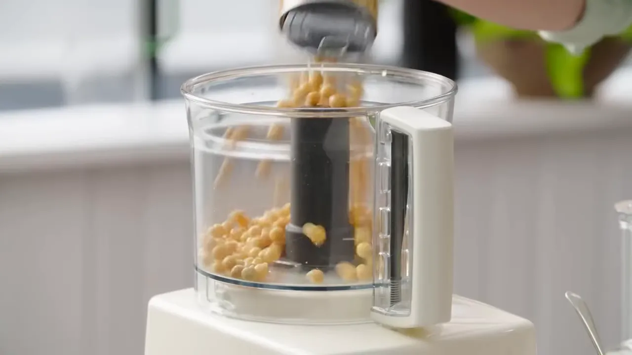 canned chickpeas being poured into a food processor bowl
