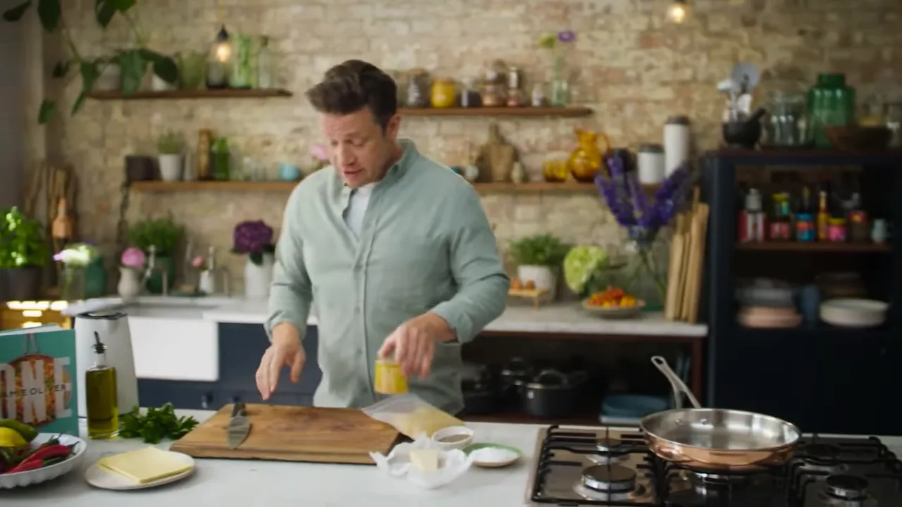 Kitchen worktop with presenter preparing ingredients: cutting board, butter, small bowls and a frying pan on the hob