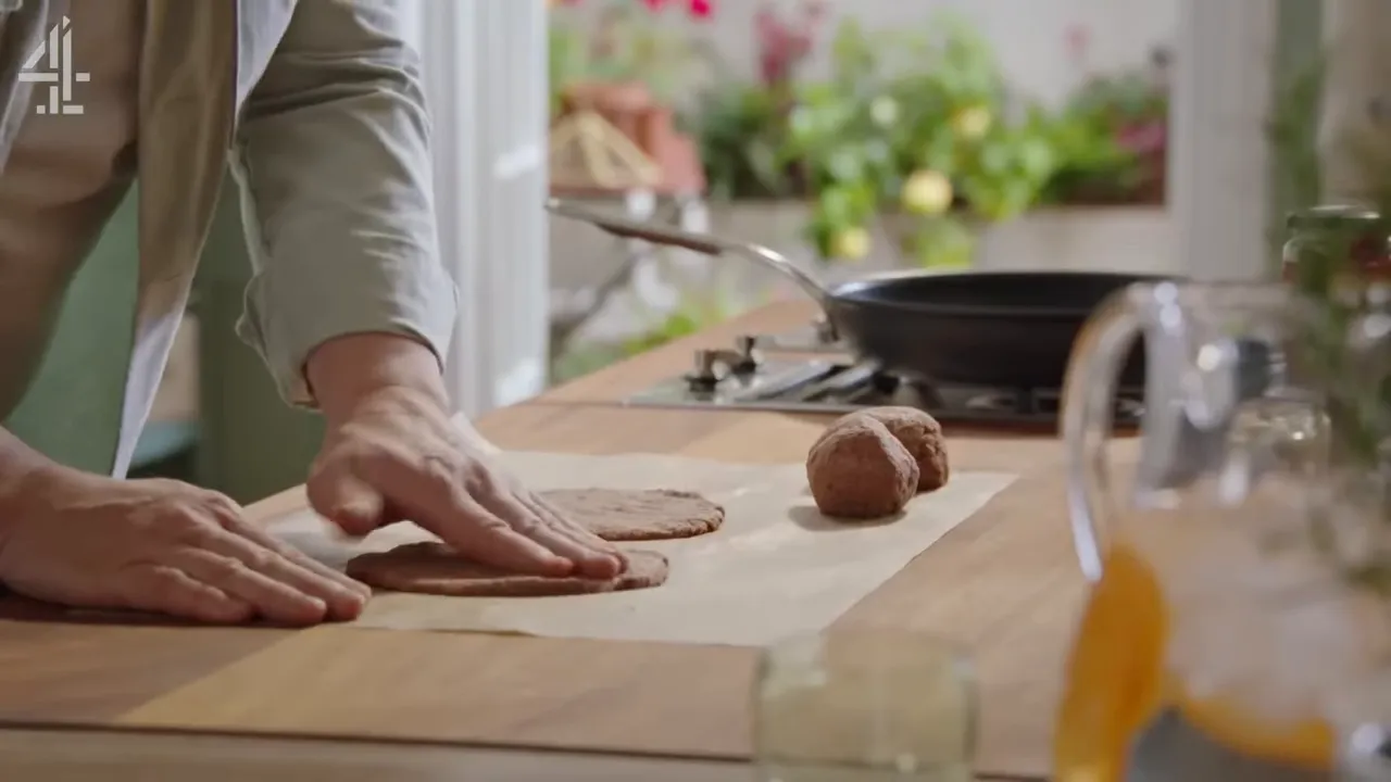 Hands pressing two flattened rounds and two dough balls on parchment with a frying pan in the background.