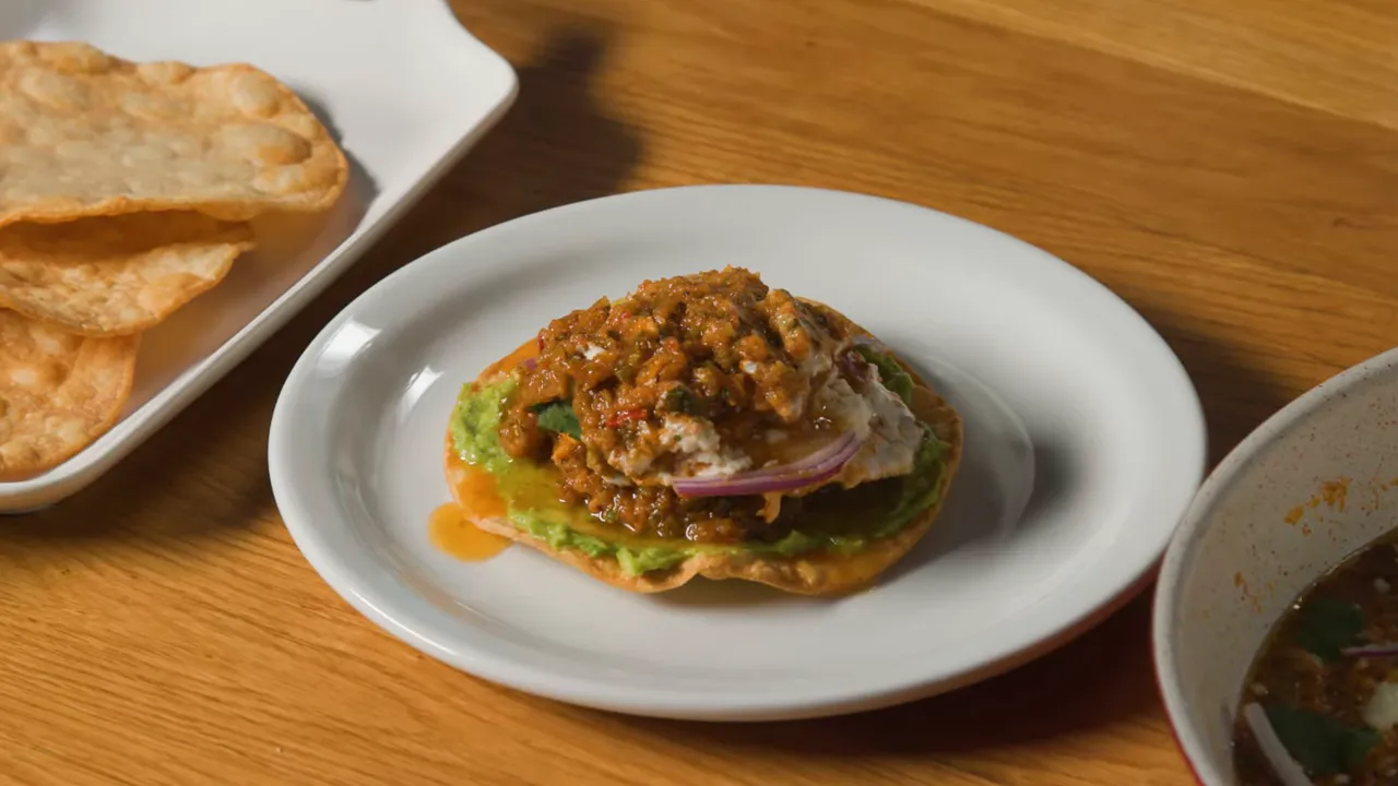 Plated tostada with avocado, egg, crema, red onion and a mound of salsa, close-up on a wooden table