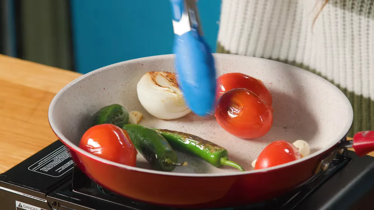 Pan with charred tomatoes, jalapeños, onion and garlic being roasted for salsa